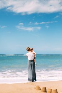 Woman carrying a baby on the beach sunny day